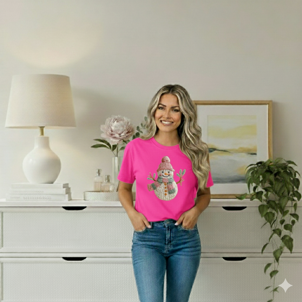 Woman wearing a pink t-shirt with a snowman design in a room with a lamp, plant, and painting.