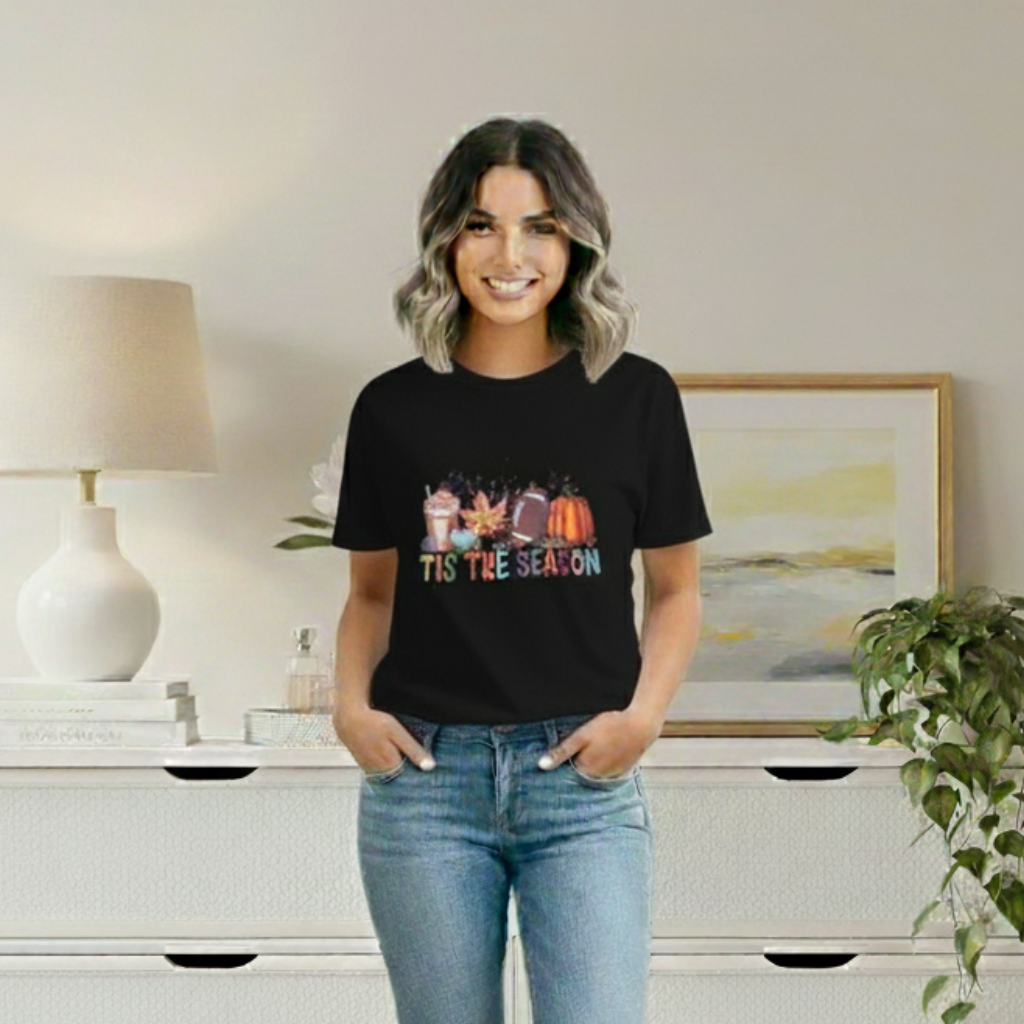 Woman wearing a black t-shirt with colorful design and text, standing in a room with a lamp and painting.